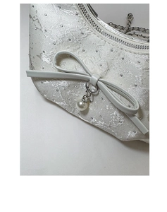 Close-up of white embroidered fabric with rhinestones, leather bow, and pearl on bag