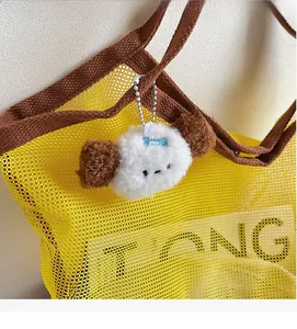 Detail of cute plush cartoon dog keychain with blue bow on yellow mesh shopping bag