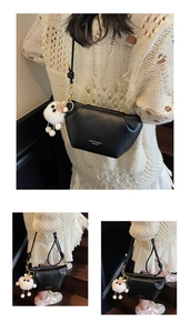 Detail of black trapezoid crossbody bag with gold zipper and white plush charm accessory