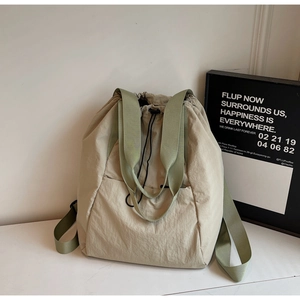 Detail of khaki nylon drawstring backpack with green straps on a white desk