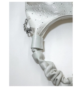 Macro detail of silver floral jacquard fabric and rhinestones on pleated handbag