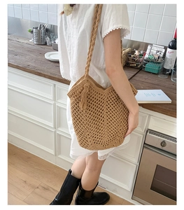 Detail of woven straw tote bag with cutout mesh pattern and decorative side tassel