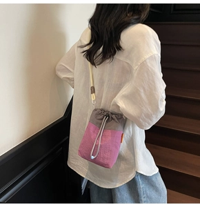 Detail of drawstring bucket bag with contrast color stitching and textured fabric on model