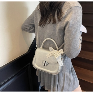 Détail du sac à main argenté métallisé avec pendentif cœur perlé et nœud en dentelle blanche