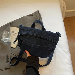 Détail du sac bandoulière en denim bleu foncé avec poignée supérieure sur un lit