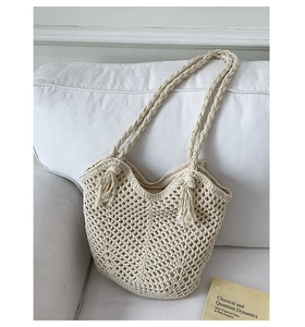 Close-up of cream crochet shoulder bag with hollow mesh pattern and fringe on a soft sofa