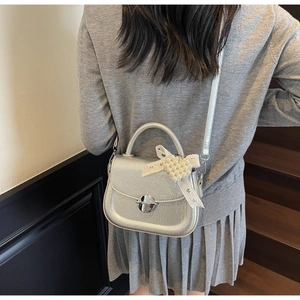 Vue détaillée du sac bandoulière argenté avec nœud en dentelle et pendentif cœur perlé