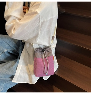 Crossbody drawstring bucket bag with pink checkered pattern shown on a female model