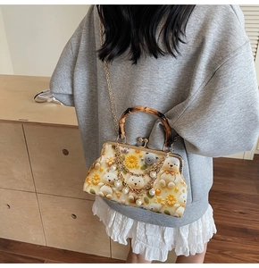 Close-up of vintage beige handbag with daisy bear pattern, bamboo handle and pearl chain