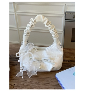 Detail of white lace handbag with pleated handle, leather bow, and pearl chain accents