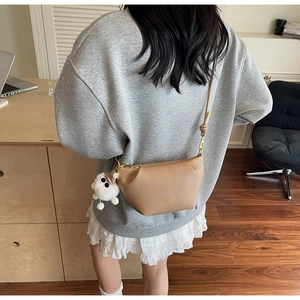 Detail of beige crossbody bag featuring golden hardware and a cute white plush pendant
