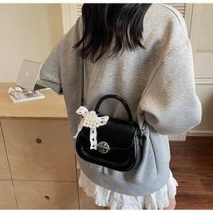 Détail du sac carré en cuir verni noir avec nœud en dentelle perlée et boucle argentée