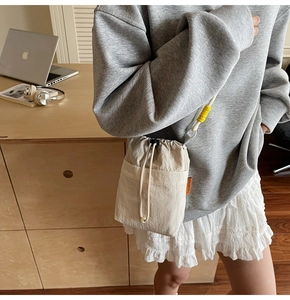 Detail of beige drawstring bucket bag with light textured fabric and yellow adjuster