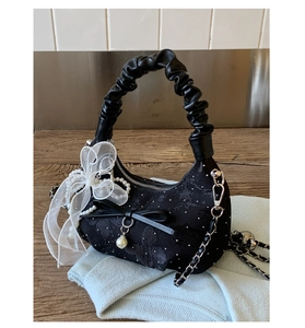 Detail of black floral jacquard handbag with organza bow and pearl charm on wooden surface