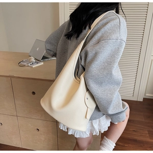 Close-up of cream lychee leather bucket bag with wide strap and metallic button detail