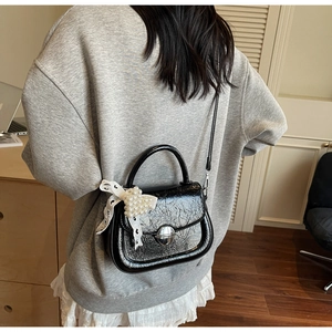 Détails du sac bandoulière en cuir verni noir avec texture vintage et nœud en perles