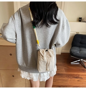 Detail view of a beige drawstring bucket bag with colorful braided cord shoulder strap