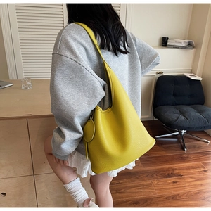 Detailed close-up of a bright yellow textured leather bucket bag with a round charm
