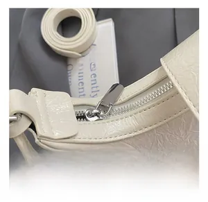 Detail showing the silver metal zipper and wrinkled texture of the ivory crescent bag