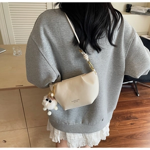 Close-up of beige crescent bag with pleated design and plush doll accessory on straps