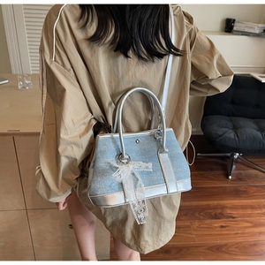 Detail of light blue denim bucket bag with silver leather trim and white lace bow accessory