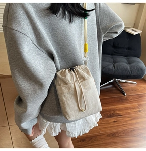 Lifestyle view of cream drawstring crossbody bag with textured fabric and colored accents