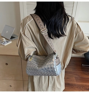 Detail of silver woven pillow bag featuring a wide jacquard strap and metallic texture