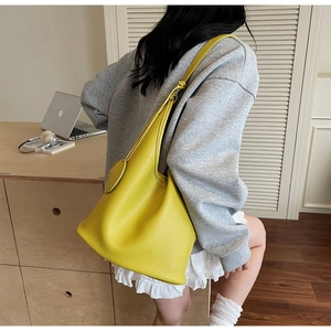 Bright yellow pebbled leather bucket bag with circular charm shown on casual model outfit
