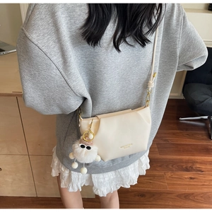 Close-up of beige dumpling bag with soft leather pleats and a cute plush ball charm