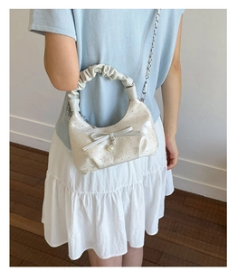 Detail of cream crossbody bag with bow, pearl charm, and stylish pleated handle