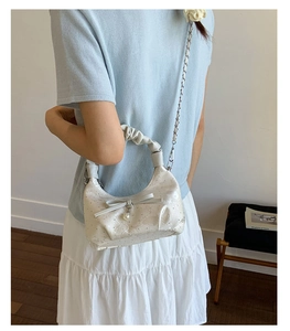 White shoulder bag featuring a decorative bow, pearl pendant, and pleated fabric handle