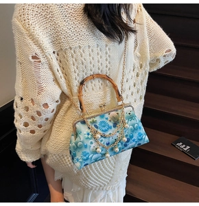 Detail view of light blue handbag with bamboo handle, pearl chain, and floral bear pattern