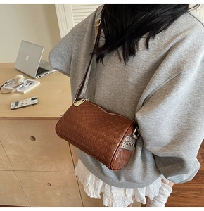Detail of dark brown woven cylinder bag with wide jacquard strap and gold zipper