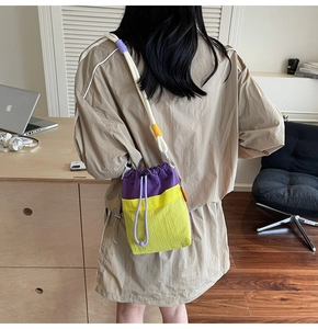 Detail of nylon bucket bag with purple and green contrast stitching and white rope strap