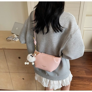 Pink crescent crossbody bag with white plush charm shown on a model in a modern office setting