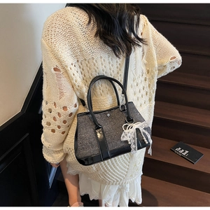 Detail of grey tweed bucket bag featuring lace bow and pearl charm on a model