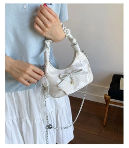 Detail of creamy white crescent hobo bag with ruffled handle, bow and pearl charm decor