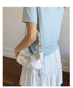 Close-up of white leather bag with bow detail, pearl charms and metal chain strap