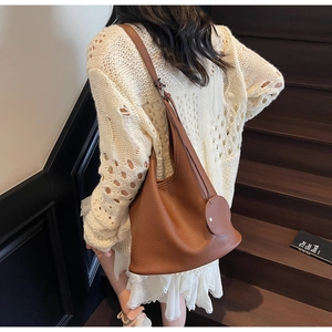 Detail of caramel lychee grain leather bucket bag with wide strap and charm on stairs