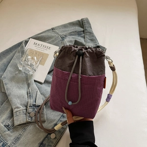 Detail of color-block drawstring bucket bag with purple checkered pattern and woven handle