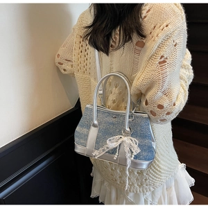 Detail of blue denim bucket bag with white lace bow and pearl pendant on a model