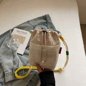 Detail of beige drawstring bucket bag featuring contrast rope strap and woven fabric texture