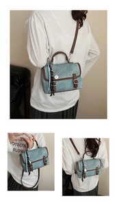 Detail of light blue stonewashed backpack with brown leather trim and metal buckles
