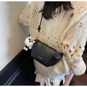 Detail of black leather crossbody bag with golden hardware and white plush lamb charm