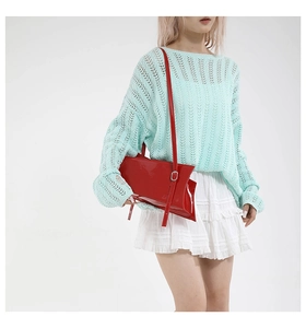 Détail du sac à bandoulière en cuir verni rouge avec pull en tricot vert et jupe blanche