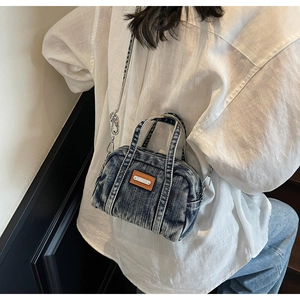 Detail of vintage washed denim mini bag with brown leather tag and metal chain strap