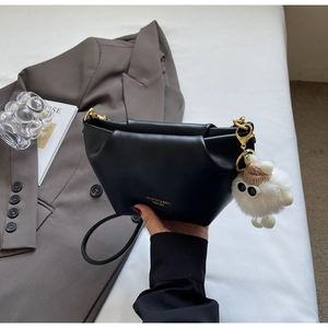 Detail of black pleated handbag with plush sheep charm and golden metal hardware