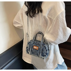 Detail of vintage denim shoulder bag showing washed blue texture and leather patch