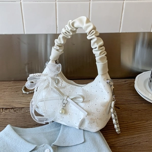 Detail of white quilted bucket bag featuring lace bow, pearl charm, and ruffled handle