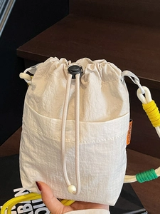 Minimalist beige drawstring bucket bag with patchwork pocket and colorful woven shoulder strap